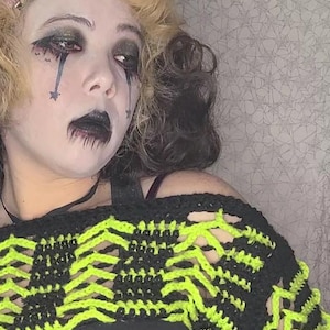 Puede incluir: Un top de crochet negro y verde neón con mangas largas y estilo corto. El top tiene un patrón geométrico y se lleva sobre una camisa negra.