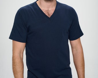 May include: A man wearing a dark blue v-neck t-shirt with short sleeves. He is standing in front of a white background.