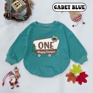 May include: Cadet blue baby sweatshirt with long sleeves. The front features a graphic of a camper with the text "ONE Happy Camper" and a bear illustration. The name "Oliver" is above the camper graphic.