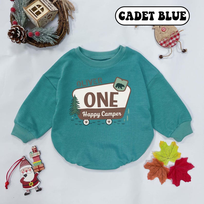 May include: Cadet blue baby sweatshirt with long sleeves. The front features a graphic of a camper with the text "ONE Happy Camper" and a bear illustration. The name "Oliver" is above the camper graphic.