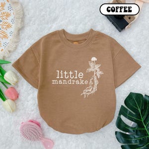 May include: A brown short-sleeved t-shirt with a white graphic of a mandrake root and the text "little mandrake".