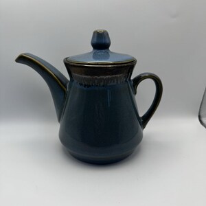 May include: A blue ceramic teapot with a brown rim and a lid. The teapot has a rounded body and a spout on one side and a handle on the other.