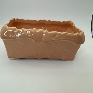 May include: A rectangular peach-colored ceramic planter with a textured basket weave design. The rim of the planter has a wavy, uneven edge. The planter is empty and sits on a white surface.