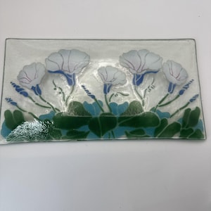 May include: Rectangular glass dish with a floral design. The dish features white flowers with blue and red accents, green leaves, and blue stems. The flowers are arranged across the top of the dish.