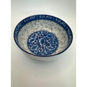 May include: A white and blue ceramic bowl with a floral design. The bowl has a blue rim with a repeating pattern and a central blue floral motif. The interior features a delicate white floral pattern.