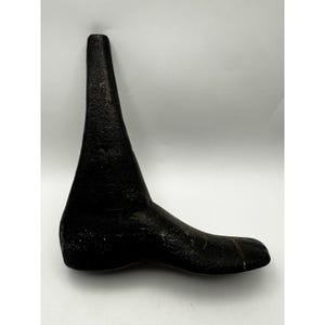 Peut inclure: Un formier de cordonnier en fonte noire, utilisé pour façonner les chaussures. La forme est en forme de pied, avec un talon pointu et une longue semelle plate. La surface a un aspect texturé.