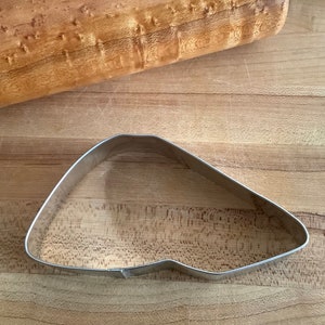 May include: A silver metal cookie cutter shaped like a pointed, curved triangle.