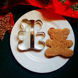 May include: A metal cookie cutter shaped like a bear, and a bear-shaped piece of bread on a white plate.