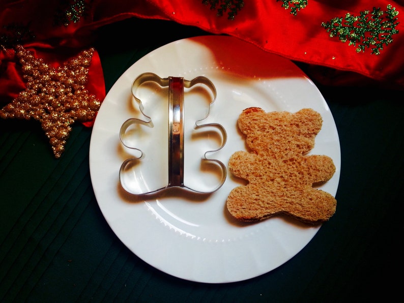 May include: A metal cookie cutter shaped like a bear, and a bear-shaped piece of bread on a white plate.