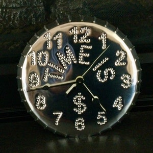 May include: A silver clock with a unique design. The numbers are made of small metal circles and the clock face is reflective. The clock hands are black.