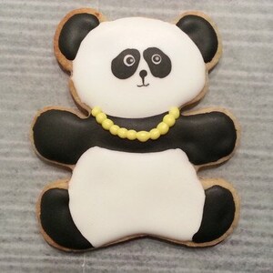 May include: A black and white panda bear cookie decorated with yellow icing. The cookie has a black nose and eyes and is wearing a yellow beaded necklace.
