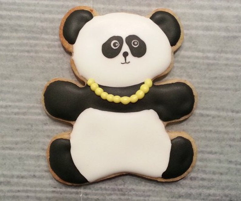 May include: A black and white panda bear cookie decorated with yellow icing. The cookie has a black nose and eyes and is wearing a yellow beaded necklace.