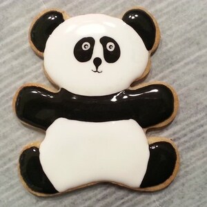 May include: A black and white panda bear cookie decorated with icing. The cookie is shaped like a bear with black ears, arms, and legs.