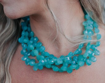 May include: A woman wearing a turquoise gemstone necklace. The necklace is made of faceted beads and is layered for a bohemian look.