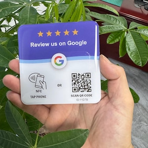 Könnte beinhalten: Ein quadratisches Schild mit glänzender Oberfläche, das im oberen violetten Bereich fünf gelbe Sterne und den Text Review us on Google zeigt. Der weiße untere Teil enthält ein Google-Logo, ein NFC-Symbol, einen QR-Code und den Text ID:11D7B.