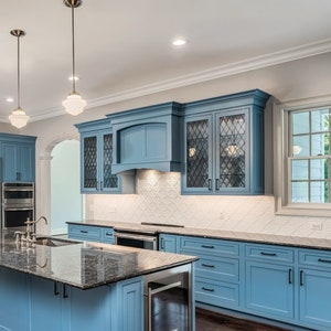 May include: A spacious kitchen with light blue cabinetry and a large island with a granite countertop. Stainless steel appliances include a refrigerator, oven, and wine cooler. Overhead, three pendant lights hang above the island.