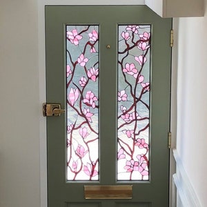 May include: A sage green front door with two glass panels featuring a pink floral design. The door has a brass handle and a mail slot. Above the door is a frosted glass panel with the letters "SI".