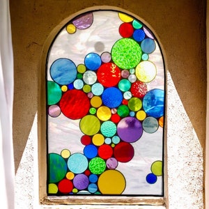 May include: A stained glass window with a design of colorful circles in various sizes and shades of red, blue, green, yellow, and purple.
