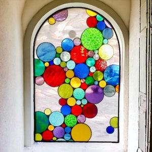 May include: A stained glass window with a design of colorful circles in various shades of red, blue, green, yellow, and purple.
