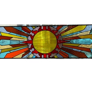 May include: A stained glass window depicting a stylized sun with radiating rays in shades of red, orange, yellow, blue, and brown.