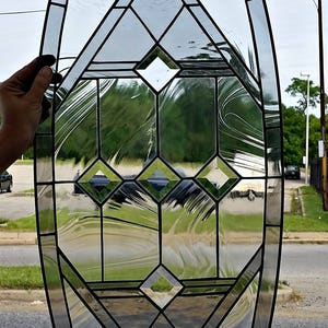 May include: A stained glass window with a geometric design in an oval shape. The glass is clear with black lead lines creating a diamond pattern.