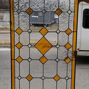 May include: A stained glass window with a geometric pattern of clear and amber glass. The window is framed in black and has a gold border.
