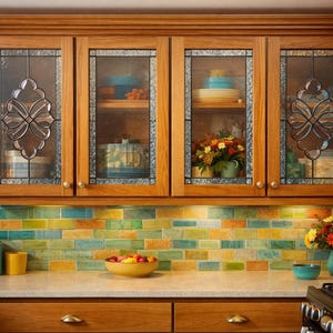 May include: Wooden kitchen cabinets with glass-front doors. The cabinets have decorative leaded glass panels. The kitchen features a colorful tile backsplash and a countertop with various kitchen items, including a toaster and a canister.