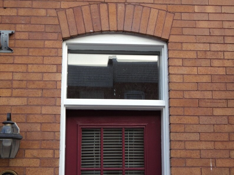 May include: A red brick building with a white window and a red door. The window has a white frame and the door has a white frame and a white paneled door with a red door handle. The door has a white window with a white frame and a white paneled door with a red door handle.