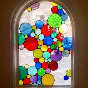 May include: A stained glass window with a design of colorful circles in various sizes. The circles are arranged in a cascading pattern, creating a whimsical and vibrant effect.