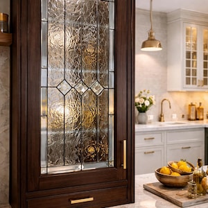 May include: Dark wood kitchen cabinet with a textured glass door. The glass is divided into rectangular and diamond shapes. Gold-toned hardware accents the cabinet. A marble countertop and other kitchen elements are visible.