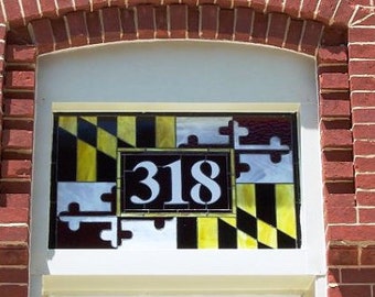 May include: A stained glass window with the Maryland state flag and the number 318. The window is set in a brick wall.