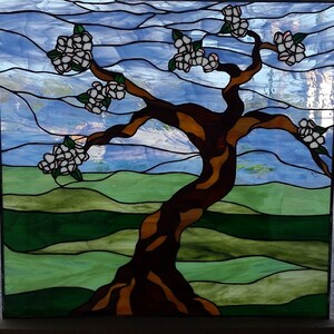 May include: A stained glass window depicting a stylized tree with white blossoms against a blue sky and green hills background.