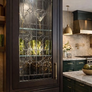 May include: Dark wood kitchen cabinet with a leaded glass door. The glass door has a decorative pattern and is filled with glassware. The cabinet has brass hardware and is set against a marble countertop.