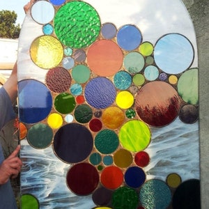 May include: A stained glass window featuring a colorful design of overlapping circles in various shades of red, green, blue, yellow, and brown. The circles are arranged in a cascading pattern, creating a visually appealing and abstract design.