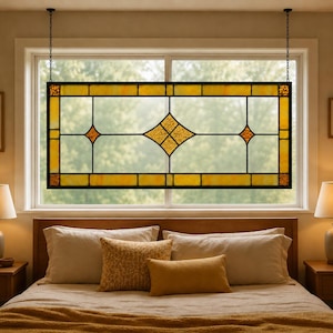 May include: A rectangular stained glass window panel with a black frame and hanging chains. The panel features a yellow and amber color scheme with diamond and square geometric designs. The window is suspended in front of a window.