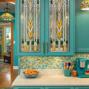 May include: Teal kitchen cabinets with stained glass doors featuring a wheat-like design in yellow, orange, and green. The cabinets have gold hardware and sit above a countertop with a mosaic tile backsplash. A bowl of oranges sits on the counter.