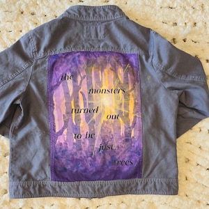 May include: A grey denim jacket with a purple and yellow watercolour design on the back. The design features trees and the text "the monsters turned out to be just trees".