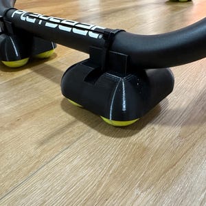 May include: Black exercise equipment with the word "PLAYSEAT" in white. The equipment has a curved black bar supported by black bases with yellow rollers. The equipment is on a light brown wooden floor.
