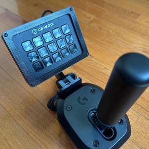 May include: A black Stream Deck with 15 buttons and a black joystick with a blue accent. The Stream Deck is mounted on the joystick.