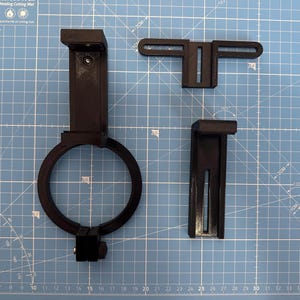 May include: Three black 3D printed parts for a phone camera mount. The parts include a phone holder, a lens adapter ring, and a bracket.