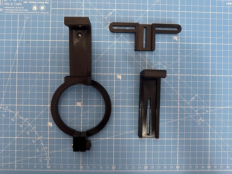 May include: Three black 3D printed parts for a phone camera mount. The parts include a phone holder, a lens adapter ring, and a bracket.