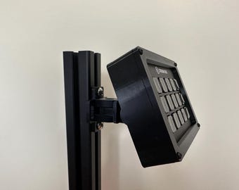 May include: A black, rectangular device with a grid of buttons, mounted on a black metal track. The device has the text "STREAM DECK" printed on it.