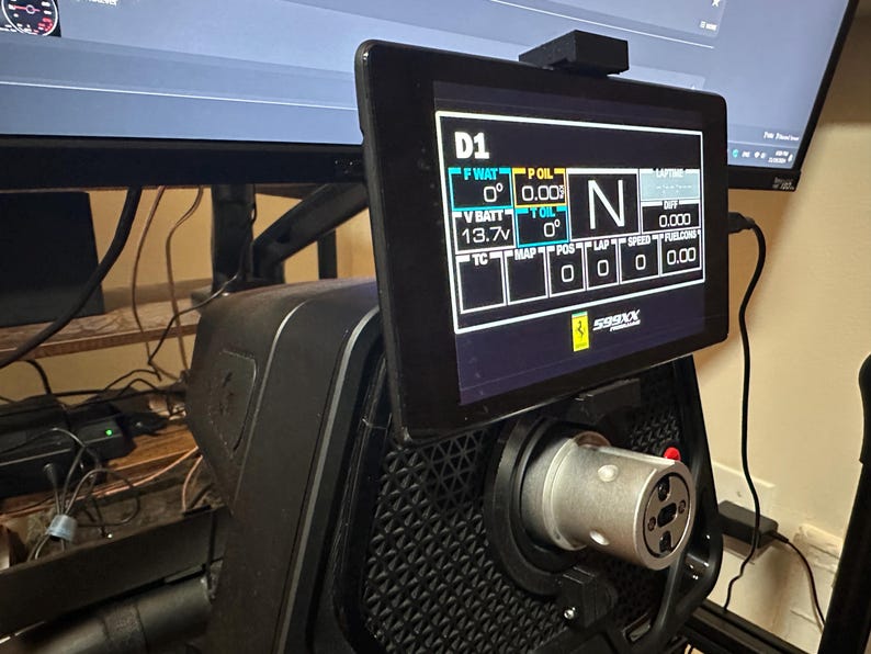May include: A black racing simulator with a tablet mounted on the steering wheel. The tablet displays data such as speed, engine temperature, and battery voltage. The text on the screen reads "D1", "F WAT", "0&deg;", "P OIL", "0.00", "T OIL", "0&deg;", "V BATT", "13.7v", "TC", "MAP", "POS", "LAP", "SPEED", "FULLCON", "0", "0", "0", "0", "0.00", "N", "0.000", "XX665".
