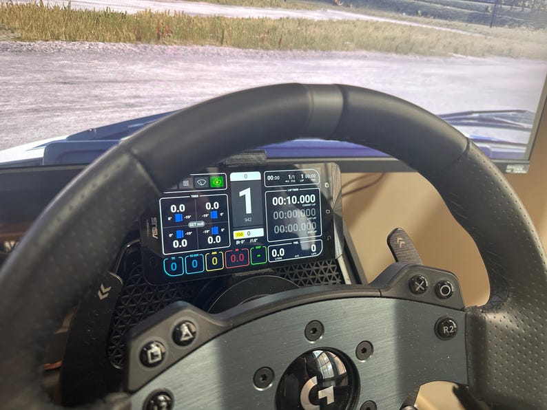 May include: A black racing steering wheel with a digital display showing a timer, lap count, and other data. The display is mounted on the steering wheel with a phone holder.
