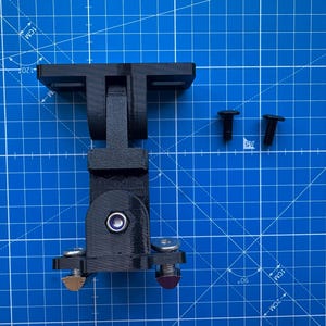 May include: A black 3D-printed articulated mounting bracket with a central hinge, a flat base with two mounting slots, and a lower plate featuring two metal screws with silver heads and two smaller metal screws with gold and purple tips.