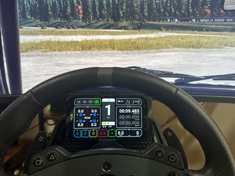 May include: A black racing steering wheel with a digital display showing a lap time of 00:09.483. The display also shows the lap number, 1, and the current gear, 1. The steering wheel has buttons and paddles for controlling the game.