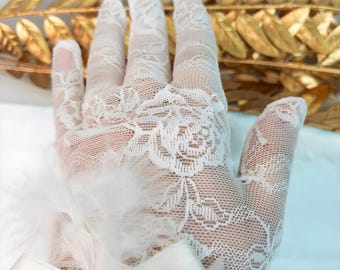 May include: A close-up of a white lace glove with a floral pattern. The glove is adorned with feathers and a satin ribbon. The background features a golden leaf arrangement, creating a delicate and elegant aesthetic.