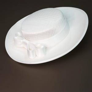 May include: A white hat with a wide brim and a decorative bow. The hat features a textured crown and a satin ribbon around the base. The bow is made of the same satin material as the ribbon.