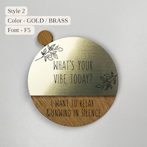 Pu&ograve; includere: Un cartello rotondo in legno e metallo dorato con il testo "What's your vibe today?" e "I want to relax & unwind in silence". Il cartello ha un design a foglie.