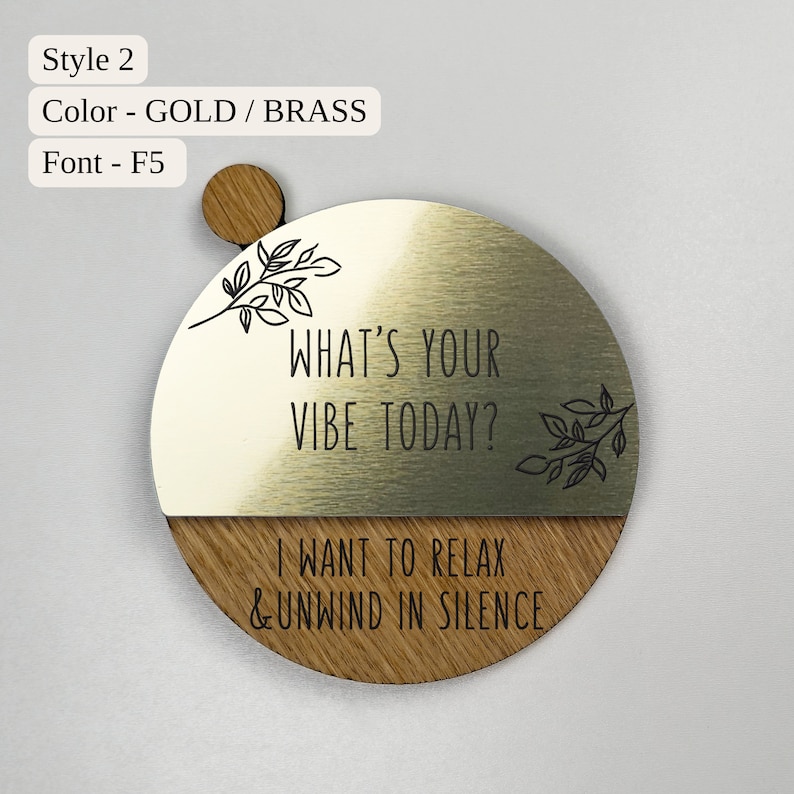 Pu&ograve; includere: Un cartello rotondo in legno e metallo dorato con il testo "What's your vibe today?" e "I want to relax & unwind in silence". Il cartello ha un design a foglie.